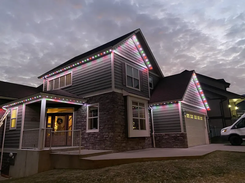 Permanent Christmas lights in red and green outlining the roofline of a two-storey home in Castlegar BC at dusk