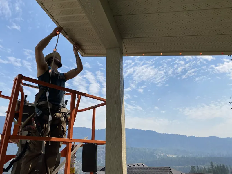 SUMMIT installer setting permanent LED lights into track from a lift above a Castlegar BC rooftop, Kootenay valley beyond