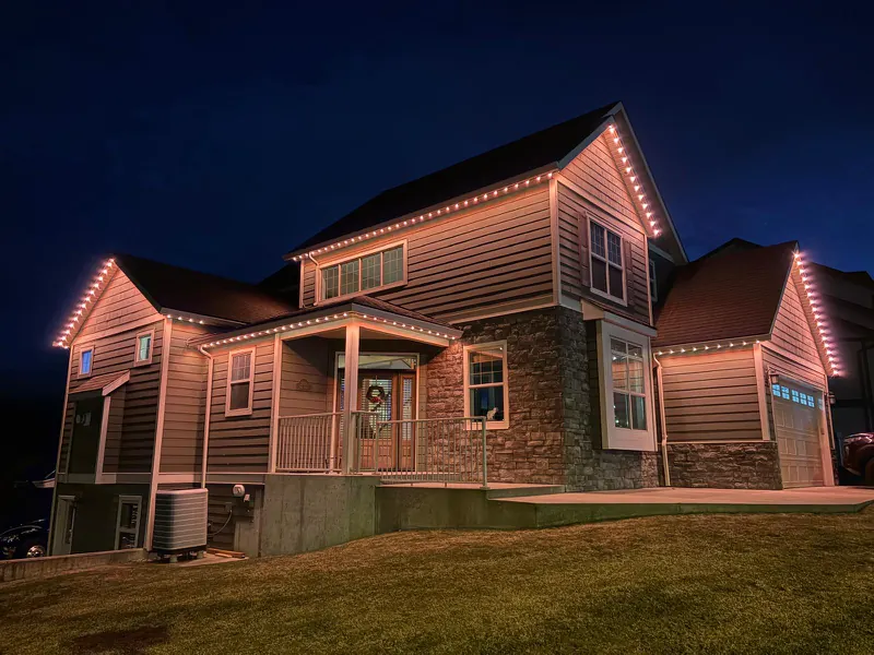 The same Castlegar BC home lit in warm white permanent roofline lighting on a clear winter evening